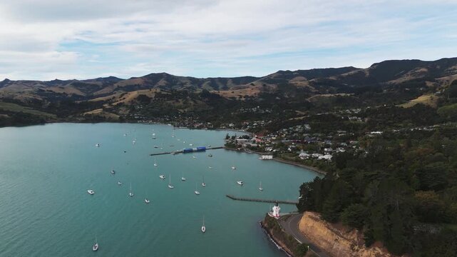 Anchored yachts and boats at beach of akaroa town. Canterbury Region, new Zealand . Aerial wide shot. Lighthouse and French bay.