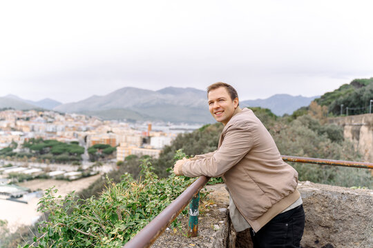 Smiling man leaning on stone wall with city and mountain view