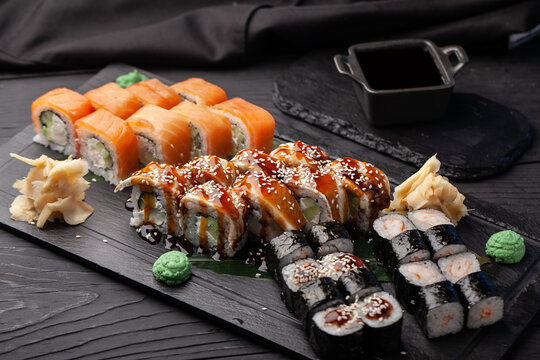 Delicious sushi platter featuring assorted rolls and garnishes served on a black slate plate - Powered by Adobe