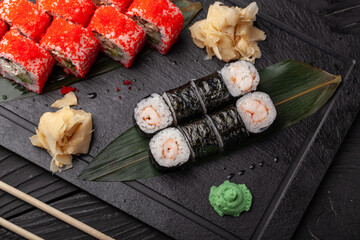 Delicious sushi rolls arranged on a black slate platter with wasabi and ginger accents