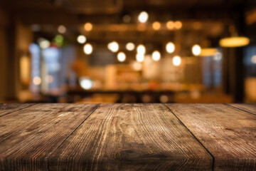 Rustic wooden table in foreground with blurred cafe interior and warm lighting in background during evening hours