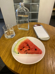 Slice of watermelon on a plate with glass bottle of water on wooden café table