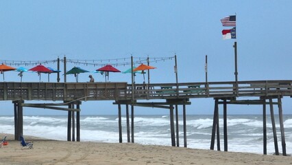 Coastal living Outer Banks, NC beach with fishing pier and waves breaking on shore with rain clouds approaching 