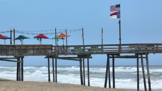 Coastal living Outer Banks, NC beach with fishing pier and waves breaking on shore with rain clouds approaching 