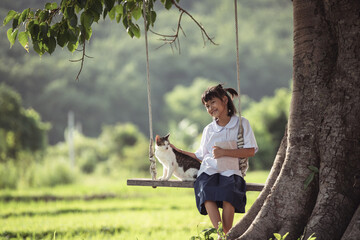 Young girl sitting on swing under tree with cat in peaceful rural landscape, enjoying nature and companionship in summer sunlight, serene atmosphere and joyful moment