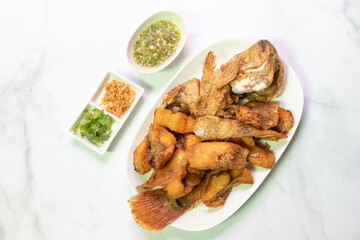 Deliciously fried Ruby fish served with spicy sauce and garnishes on a white plate, perfect for a delicious meal or restaurant menu.