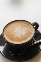 Hot coffee with milk in a black cup on white table.