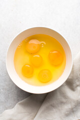 Organic raw eggs in a white mixing bowl for baking, top view of whole raw eggs on white background
