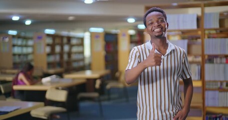 African young adult gen z man happy student standing indoor library look camera show thumbs up hand sign ready for exam smiling smart boy staring cam do pose enjoy day time inside college - Powered by Adobe