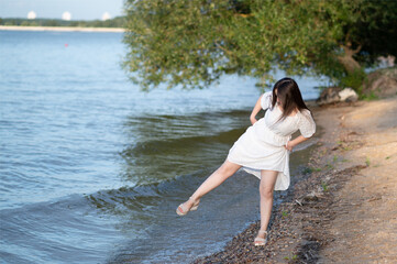 Woman in white dress walking barefoot along the shoreline, enjoying nature and water on a peaceful summer evening