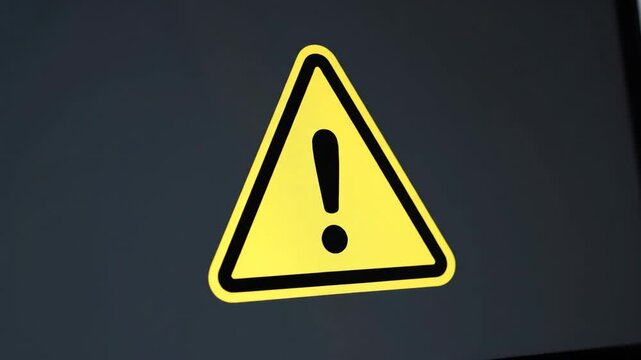 Warning Alert Symbol on Laptop Screen - Close-up view of a bright yellow warning triangle with a black exclamation mark displayed on a dark gray laptop screen.