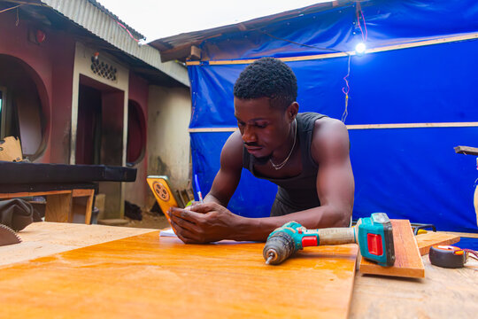 Young African carpenter writing measurements using a smartphone
