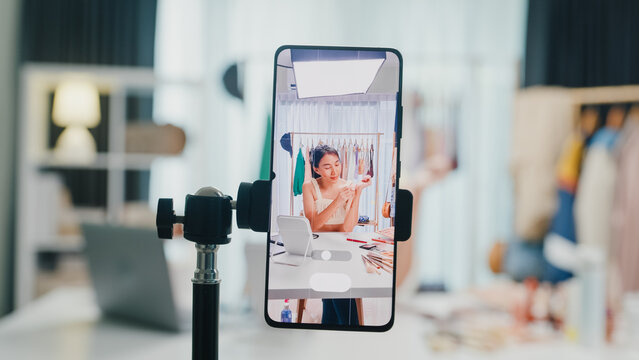 Close-up phone screen record Asia lady vlogger look phone camera apply lipstick on skin live sale online viral video selfie in IG story reel tiktok at home studio. Business online media concept.
