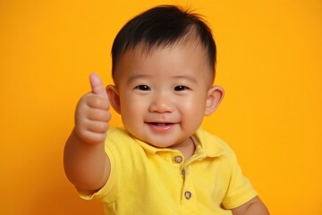 A cheerful baby in a yellow shirt gives a thumbs-up against a bright yellow background, radiating happiness and positivity.