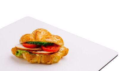 Fresh croissant sandwich with turkey, lettuce, and tomato on white plate