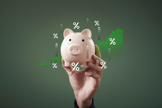 A hand holds a piggy bank surrounded by upward-trending graphs and percentage symbols, symbolizing financial growth and savings.