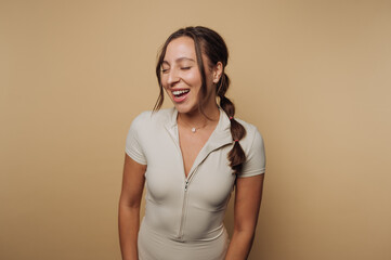 Obraz premium Smiling woman wearing a light-colored outfit in a studio with warm backdrop enjoying a joyful moment
