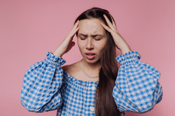 Woman experiences discomfort while touching her temples against a pink backdrop during a stressful moment