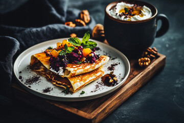 Fluffy pancakes are stacked high, adorned with vibrant fruit compote and fresh toppings, accompanied by yogurt in a rustic bowl, all set on a wooden table