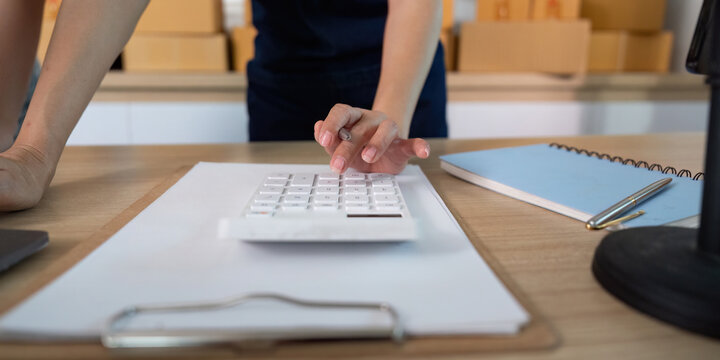 E-commerce. Close-up of a woman using a calculator for inventory management. - Powered by Adobe