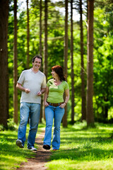 Fototapeta premium A happy mature couple strolling through a leafy forest path smiling and enjoying a sunny summer's day outdoors. From a series of images.