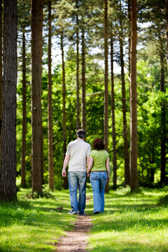 A mature couple walking away from the camera down a peaceful woodland path. They are holding hands enjoying time together on a sunny summer's day. From a series of images.