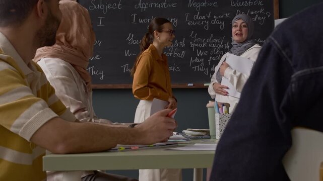 Diverse students and teacher discussing grammar sentences written on chalkboard during interactive language lesson in modern classroom