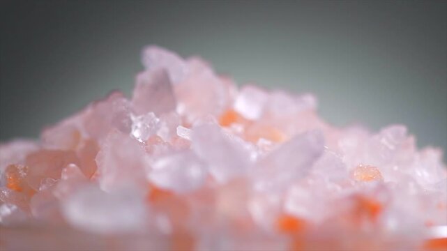 Himalayan salt, pink Himalayan salt crystals close up. Pink coarse salt crystals macro shot, rotating over grey background, slow motion video. 