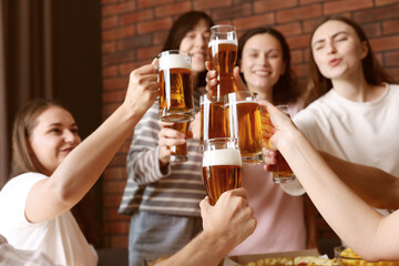 Group of happy friends clinking glasses of beer at table indoors, selective focus