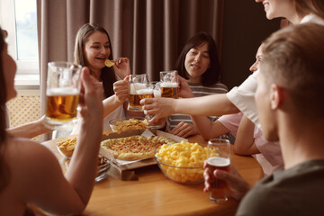 Group of happy friends clinking glasses of beer at table indoors