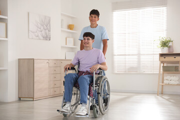 Happy young man in wheelchair and caregiver indoors