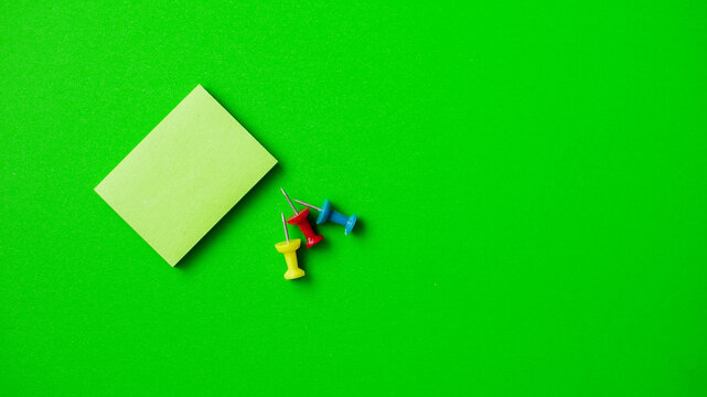 Colorful push pins and sticky note on a bright green background