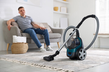 Fototapeta premium Man resting on sofa at home, focus on vacuum cleaner