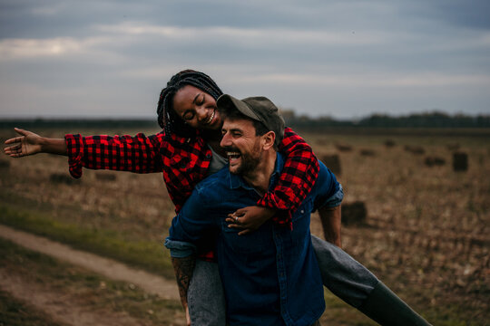 Happy farmers couple piggybacking in cultivated field at sunset - Powered by Adobe