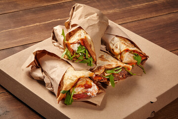 Delicious wraps with meat and vegetables filling takeaway box on wooden table