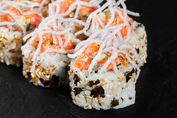 Delicious sushi rolls decorated with crispy rice noodles and salmon on black background