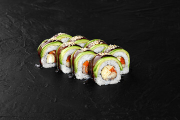 Green dragon sushi rolls with unagi, avocado, and sesame seeds on black background