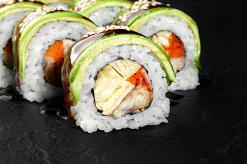 Dragon rolls covered with avocado and sesame seeds resembling green dragons resting on a black stone surface