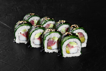 Green sushi rolls with unagi sauce and sesame seeds resting on dark stone surface