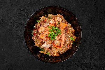 Salmon fried rice with green onions and sesame seeds in black bowl
