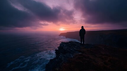 Fototapeta premium Silhouetted figure overlooking a dramatic sunset seascape