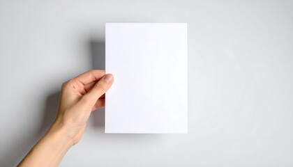 Fototapeta premium Hand Holding Blank White Paper Sheet Mockup Against Neutral Background