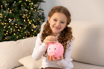 Banking, finances, investment and happy people concept. Cute happy little girl sits on sofa and...