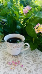porcelain cup of espresso coffee on stone table against background of flowering bush