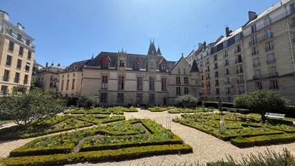 Paris, France – July 4, 2025: The Hôtel de Sens, a historic medieval building with a manicured garden, under a clear blue sky.  © Jessica