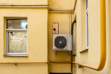 Conditioner. dirty air conditioner unit is mounted on yellow wall. ventilation and cooling of home or office during hot weather. installation and maintenance of fan air conditioner. summer heat