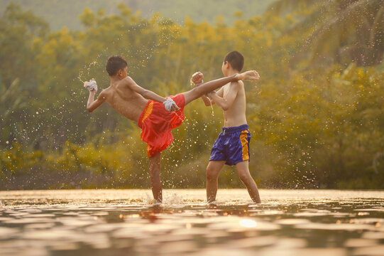 Two shirtless boys in shorts with bandaged hands doing Thai Boxing training in a river, Thailand