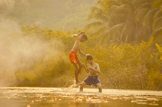 Two shirtless boys in shorts with bandaged hands doing Thai Boxing training in a river, Thailand
