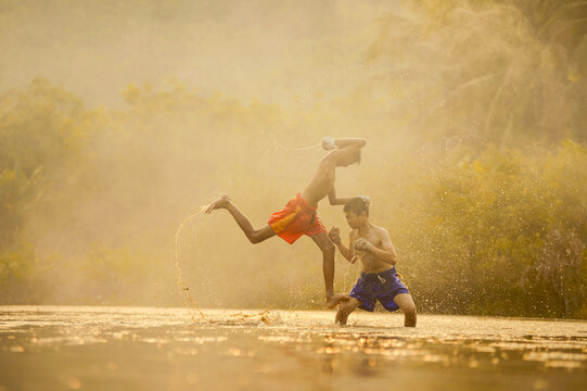 Two shirtless boys in shorts with bandaged hands doing Thai Boxing training in a river, Thailand