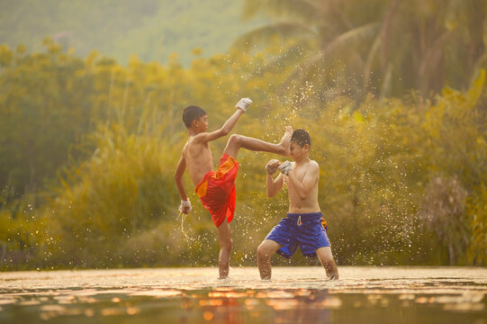 Two shirtless boys in shorts with bandaged hands doing Thai Boxing training in a river, Thailand